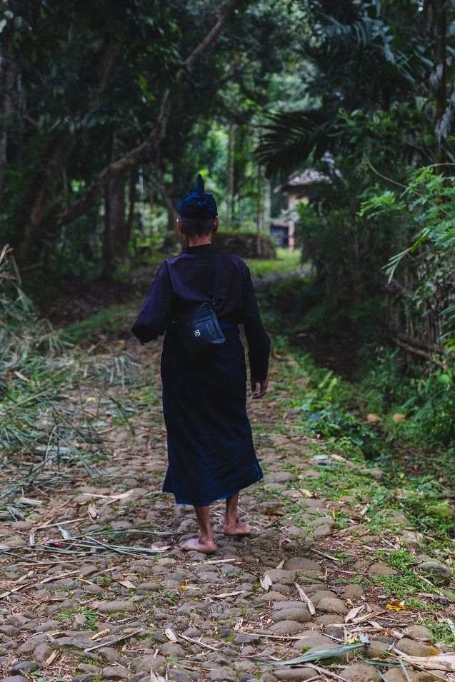 A Kajang man in black traditional dress walking a stone path into the forest